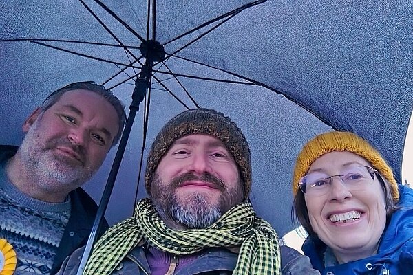 Jon Bennett, Stephen Pimm and Isabelle McKenzie under an umbrella while canvassing in Dunchurch