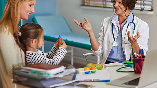 A mother holding a child whilst a GP speaks to them