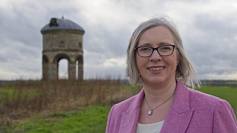 Jenny standing on a hill top with Chesterton Windmill behind her to the left